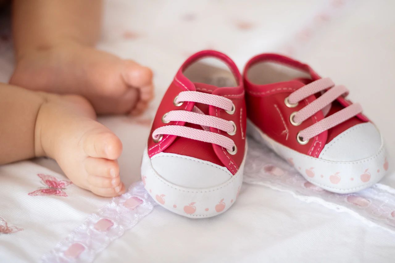 Zapatitos rosas junto a los pies de un bebé sobre una colcha clara