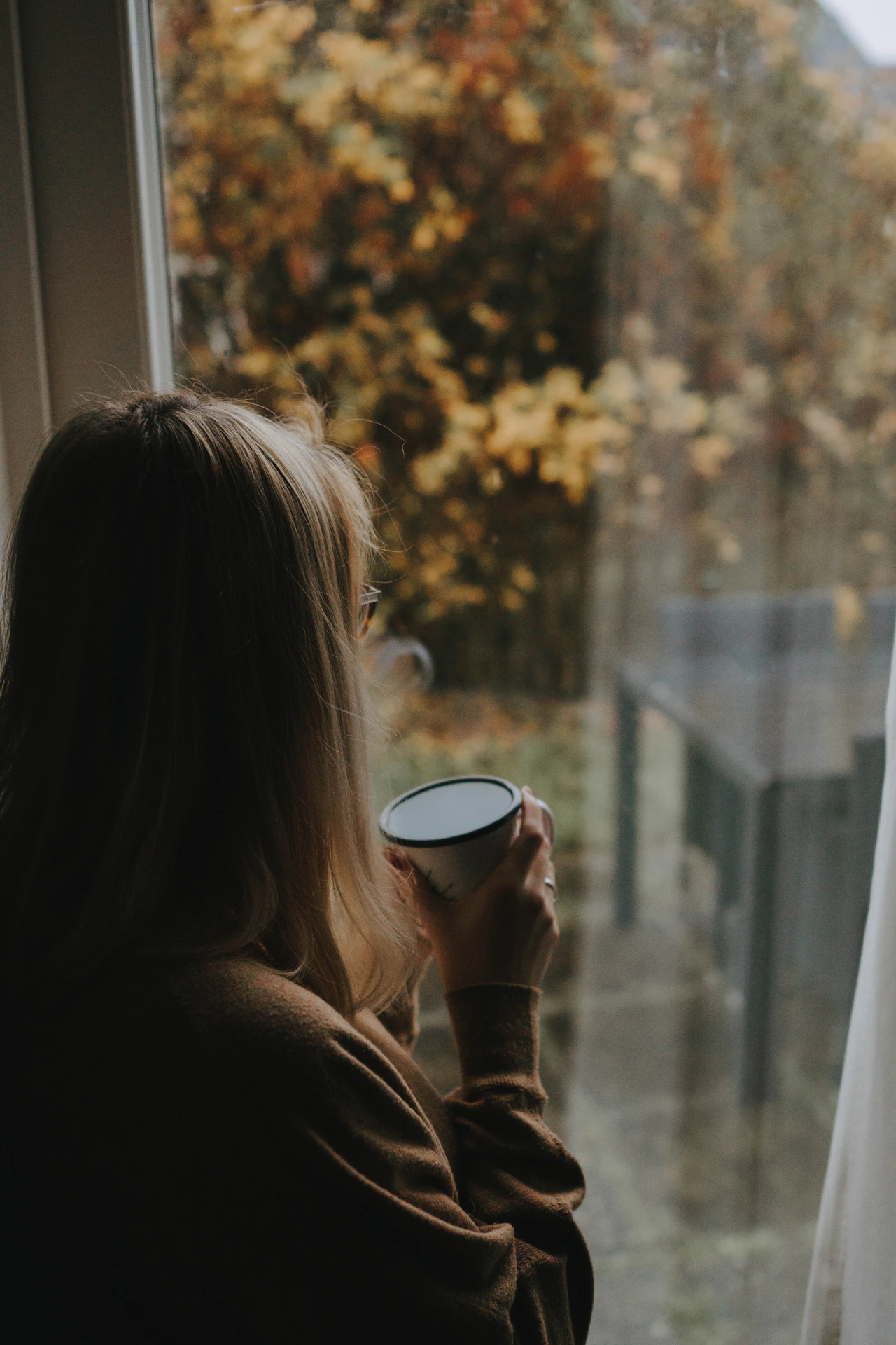Mujer con una taza junto a una ventana con vistas a árboles